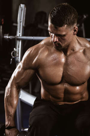 Fitness in gym, sport and healthy lifestyle concept. Handsome athletic man with naked torso making exercises. Bodybuilder male model trains deltoid muscles with dumbbells. Heavy barbell on backgroundの写真素材