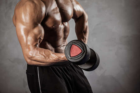 Fitness in gym, sport and healthy lifestyle concept. Handsome athletic man with naked torso making exercises. Bodybuilder male model training biceps muscles with dumbbell. No head, only bodyの写真素材