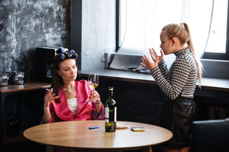 Alcoholism in family problem. Daughter aguring with her mother about drinking wine. Two people, woman and teenage girl quarrel in the kitchen. A depressed female is addicted to alcohol at home.の写真素材