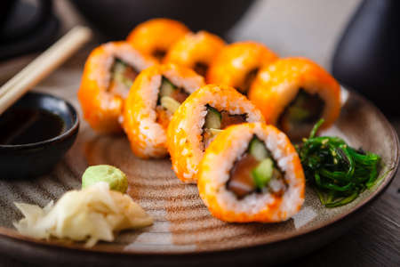 Sushi maki rolls with salmon, avocado, cucumber, flying fish roe on a plate with chopsticks, soy sauce, wasabi and ginger. Japanese traditional food served for lunch in modern gourmet restaurantの写真素材