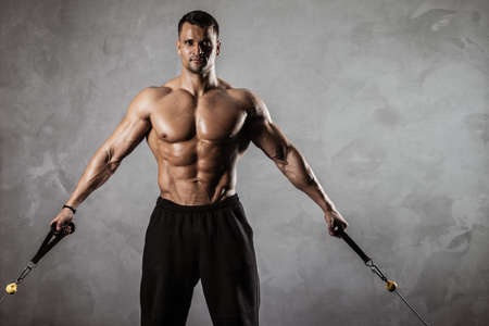 Fitness in gym, sport and healthy lifestyle concept. Handsome athletic man with naked torso making exercises. Bodybuilder male model pumping up muscles on crossover training apparatusの写真素材
