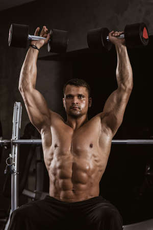 Fitness in gym, sport and healthy lifestyle concept. Handsome athletic man with naked torso making exercises. Bodybuilder male model training muscles lifting large dumbbells upの写真素材