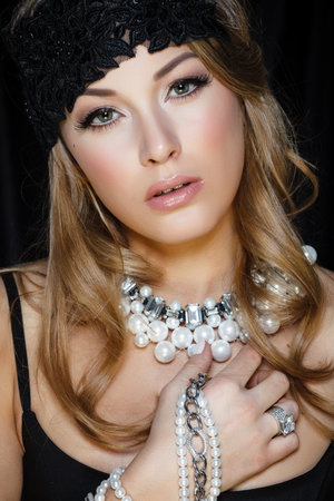 Perfect beauty and jewelry concept. Portrait of beautiful female model wearing ring, necklace and wristband on black background. Young blond woman shows glamorous fineryの写真素材