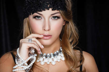 Perfect beauty and jewelry concept. Portrait of beautiful female model wearing ring, necklace and wristband on black background. Young blond woman shows glamorous fineryの写真素材