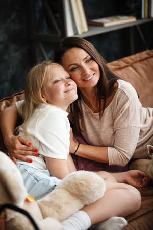 Mother and daughter relationship concept. A woman and a teenage girl are sitting in front of the TV on the couch and have fun talking. The family spends time at home. Little dog lying on lapsの写真素材