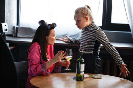 Alcoholism in family problem. Daughter aguring with her mother about drinking wine. Two people, woman and teenage girl quarrel in the kitchen. A depressed female is addicted to alcohol at home.の写真素材