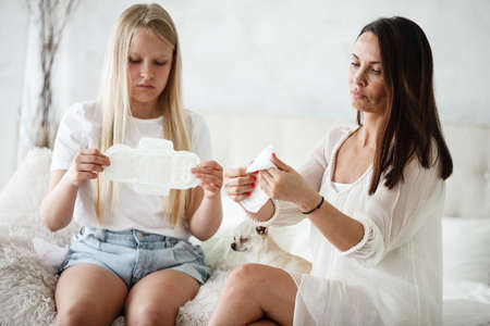 Woman hygene concept. Periods. Menstrual cycle. Mother explains daughter how to use hygiene pads and tampons. Woman and teenage girl talking at home.の写真素材