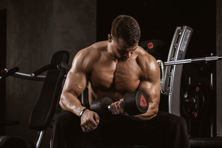 Fitness in gym, sport and healthy lifestyle concept. Handsome athletic man with naked torso making exercises. Bodybuilder male model training biceps muscles with dumbbellの写真素材