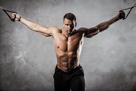 Fitness in gym, sport and healthy lifestyle concept. Handsome athletic man with naked torso making exercises. Bodybuilder male model pumping up muscles on crossover training apparatusの写真素材
