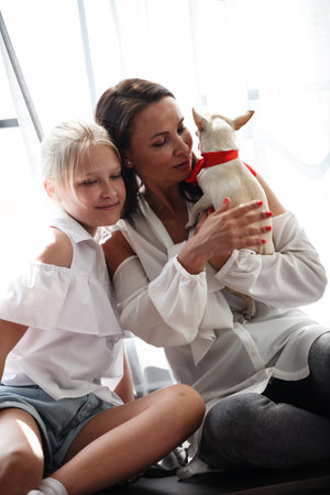 Mother and daughter relationship concept. A woman congratulates happy teenage girl on her birthday and gives her a dog as a gift. The family celebrates anniversary at home.の写真素材