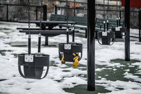 Empty playground and swings with forgotten yellow toy in winterの写真素材