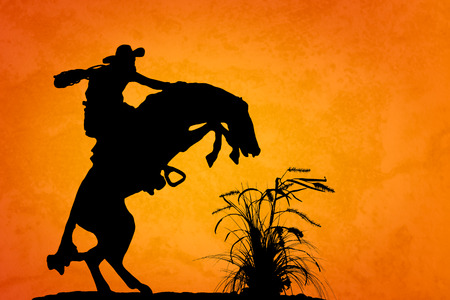 Silhouette of cowboy reigning bucking bronco spooked by something in the nearby sagebrush  Sunset orange yellow textured background の写真素材