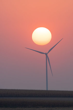The morning sun rises over a farmland windmill.