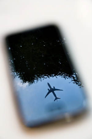 plane reflection on mobile phone with blue sky and treeの写真素材