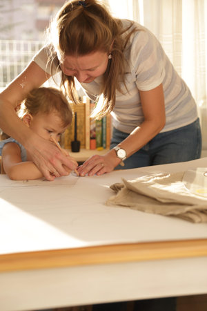 Beautiful woman working in her home with her little cute girl and cutting dress patterns