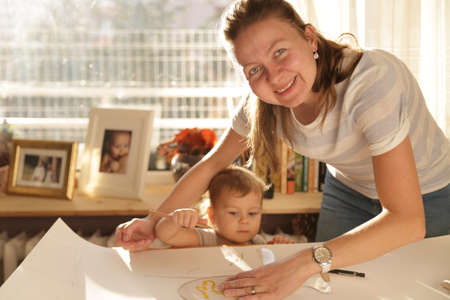 Beautiful woman working in her home with her little cute girl and cutting dress patternsの写真素材