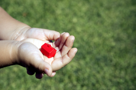 baby hands holding a red house with green backgroundの写真素材