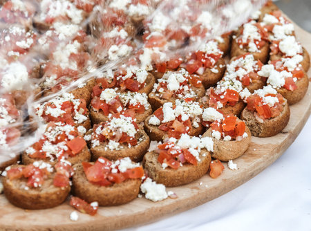greek canapes with tomatoes on dark bread on a wooden tray