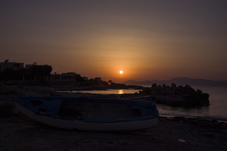 Amazing sunset on the Mediterranean Sea, view of Athens from the island of Aegina. Salty beach and a boat on the shore.の写真素材