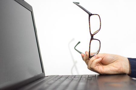 Girl holding glasses in hands leaning on the laptop while she is takingsome restの写真素材