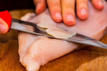 Woman cutting the chicken breast by knife on the wooden boardの写真素材