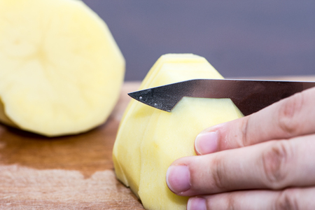 The woman cutting the peeled potato on the slices preparing for the mealの写真素材