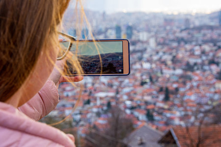 Girl with glasess and brown hair photographing cityscape of Sarajevo capital of BiH with mobile...