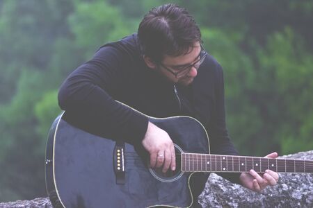 Young man playing guitar leaning against the old Roman bridgeの写真素材