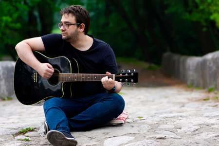 Young man playing guitar sitting on the bridge