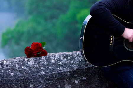 Romantic scene of man playing guitar leaning against the bridgeの写真素材