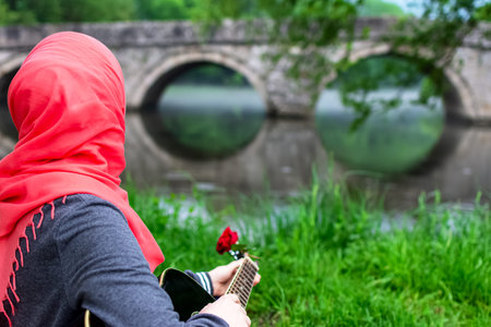 Muslim girl playing guitar and looking towards the bridge
