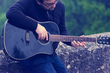 Young man playing guitar leaning against the old Roman bridgeの写真素材