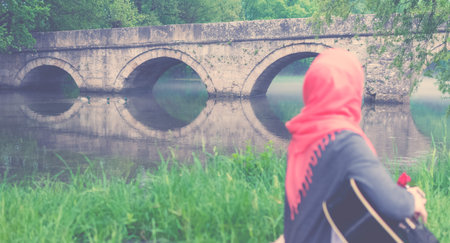 Muslim girl playing guitar and looking towards the bridge