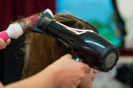 Beautiful teen girl at the hairdresser blow drying her hair after cutting itの写真素材