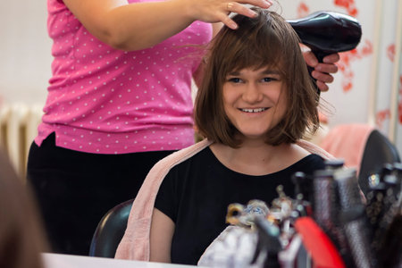 Portrait of young girl in hair salon while female hairdresser is drying her hair