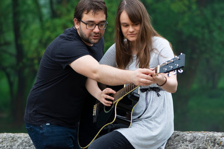 Older brother teaching his younger sister to play guitar in the nature. Beautiful moments spent...