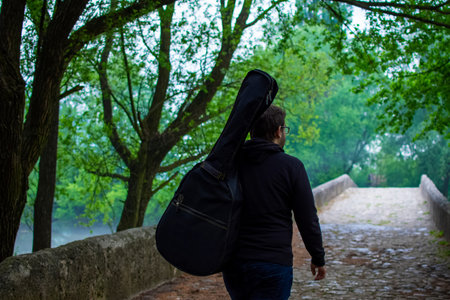 Young man carry guitar bag while walking alone through the forest. Enjoying in nature beauty