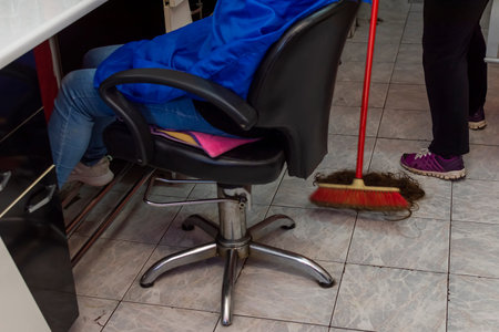 Woman cleaning floor of cut hair after customer