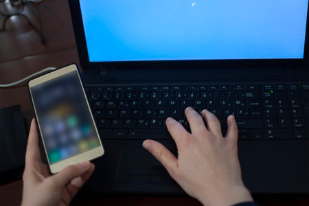 Woman's right hand on the laptop keyboard and holding mobile phone in the left hand. Laptop turning...