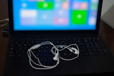 White headphones on the black laptop keyboard. Blurred half laptop display. External hard drive behind laptop on the wooden tableの写真素材