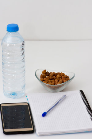 Notes, pen, smart phone, water botlle and the glass bowl filled with hazelnuts isolated on white background. Students stuff prepared for studying. Healthy lifestyleの写真素材