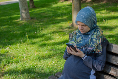 Muslim pregnant woman using smartphone in the park. Looking serious while texting message or...