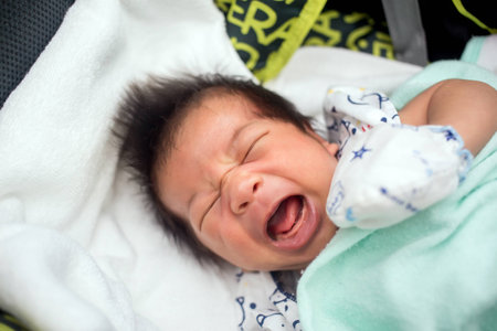 A cute one month old newborn baby is laying on her back in the crib, crying.の写真素材