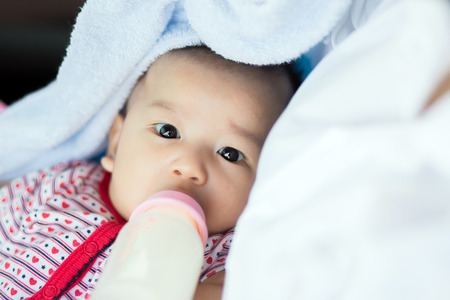 beautiful mother feeding baby boy with a milk bottle at homeの写真素材