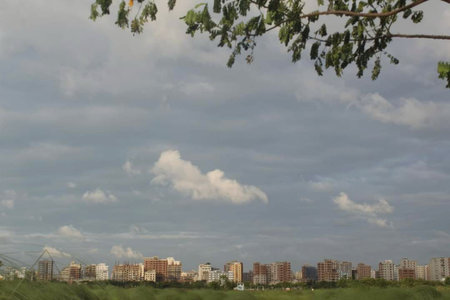 Cityscape with a cloudy sky, green grass and trees in the foregroundの写真素材