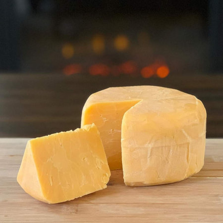 Piece of hard cheese on a wooden table in front of a fireplaceの写真素材