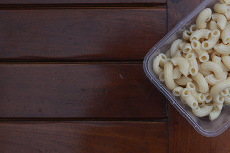a close up of boiled macaroni in a transparent container on natural patterned wood. Food concept...