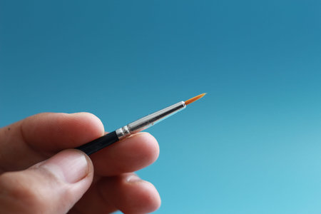 a close up of a hand holding a painting brush isolated on a blue background. concept photo art.