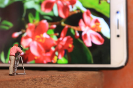 a miniature figure of a videographer filming flowers on a cell phone.の写真素材