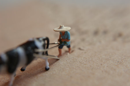 miniature figure of a farmer plowing a field with his cow on a cardboard.の写真素材